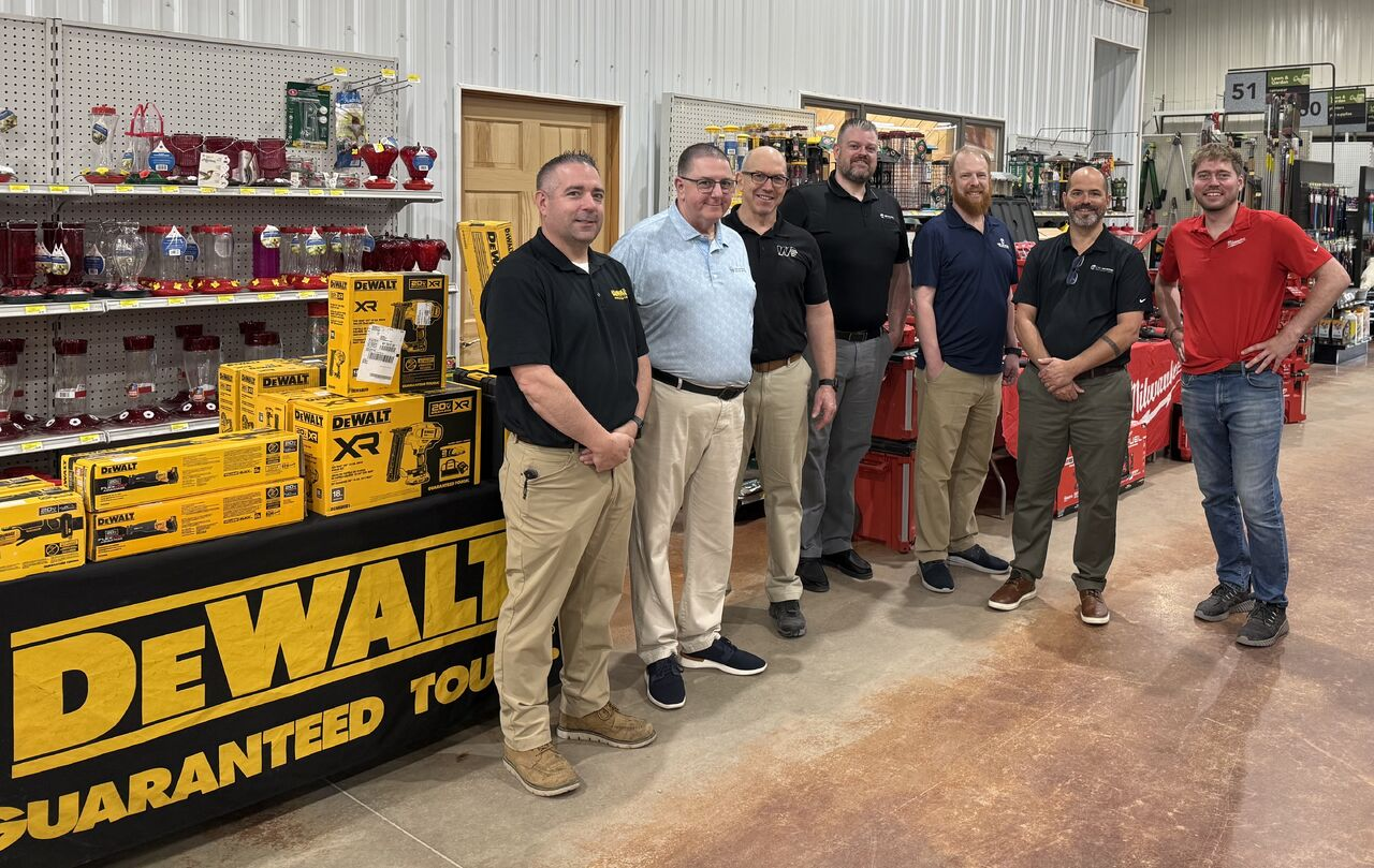 Vendor and dealer representatives standing together beside a display of power tools at a home center